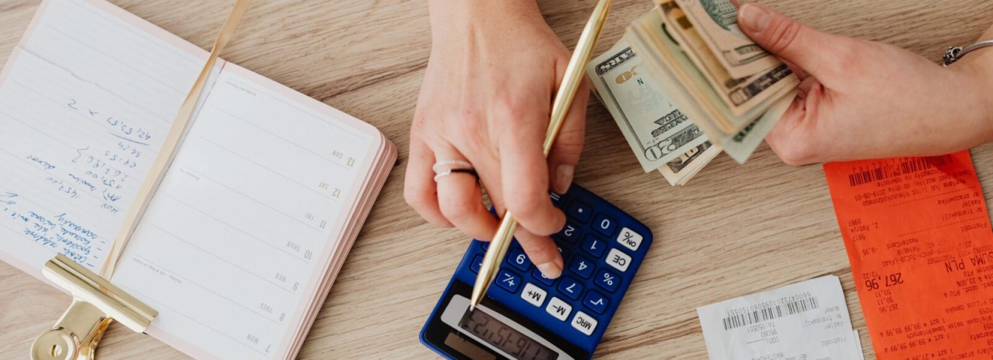 Hands managing finances with calculator, cash, and receipts on a wooden table. Ideal for budgeting concepts.