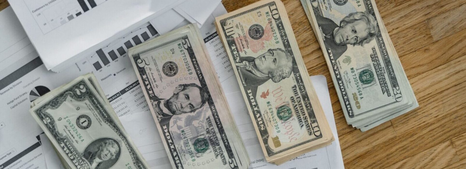 Stacks of US Dollar banknotes placed over financial documents and reports on a desk.