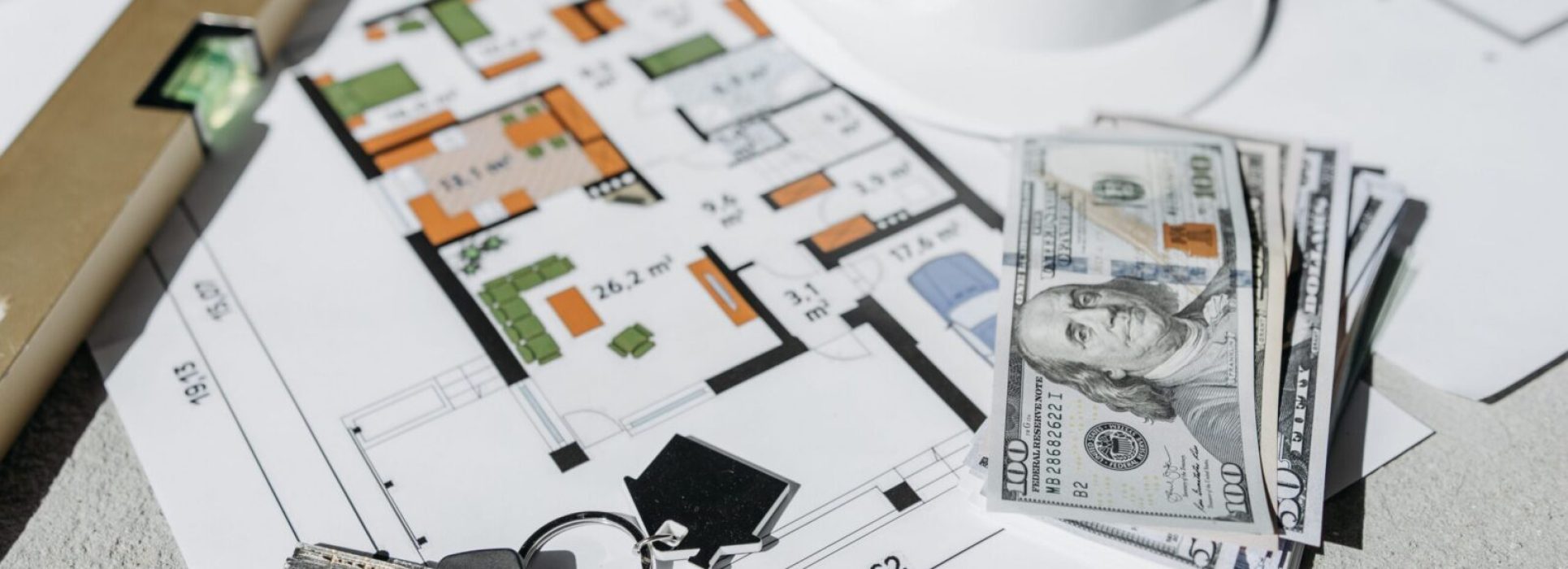 Floor plan with cash, keys, and hard hat symbolizing real estate investment and property planning.
